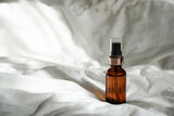 Cosmetic amber glass bottle with essential oil on white bed background with sunlights