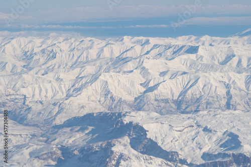 Wing of aerial view of an airplane jet flying above clouds from the window in traveling and transportation concept. White snow mountain in winter season. Nature landscape background.