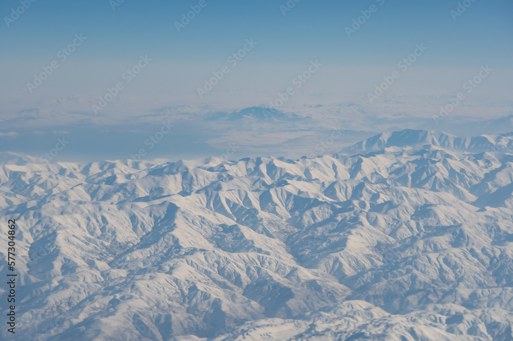 Obraz premium Wing of aerial view of an airplane jet flying above clouds from the window in traveling and transportation concept. White snow mountain in winter season. Nature landscape background.