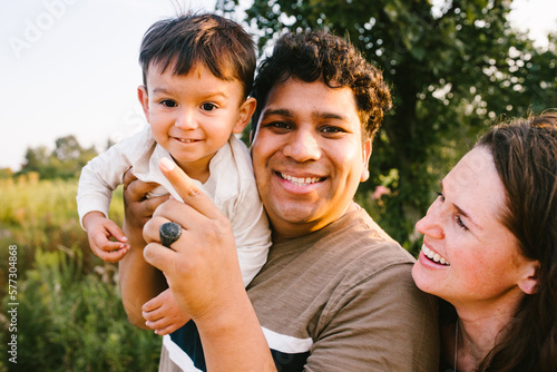 Hispanic dad holds and plays with son while mom laughs outdoor photo