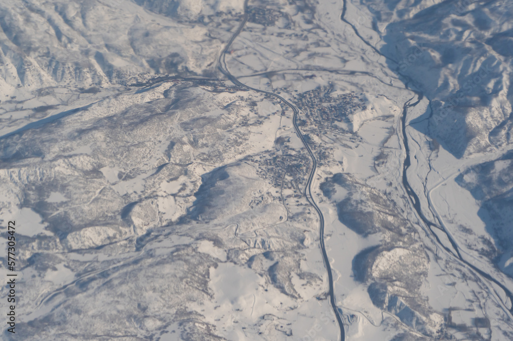 Fototapeta premium Wing of aerial view of an airplane jet flying above clouds from the window in traveling and transportation concept. White snow mountain in winter season. Nature landscape background.