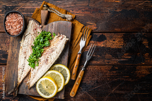 Delicious baked mackerel fillets with greens, garlic and lemon on wooden board. Wooden background. Top view. Copy space