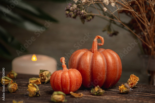 Two cute handmade pumpkin shaped candles on a wooden background with flowers  a fired white candle at the back. Cozy atmosphere