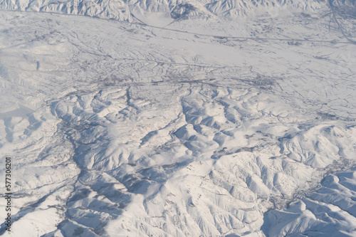 Wing of aerial view of an airplane jet flying above clouds from the window in traveling and transportation concept. White snow mountain in winter season. Nature landscape background.