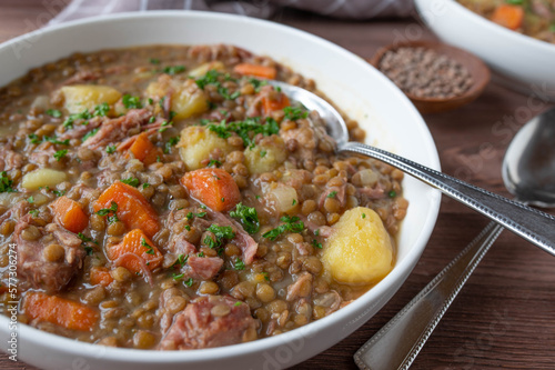 Lentil stew or soup with brown lentils, vegetables, potatoes and pork meat on a plate with spoon