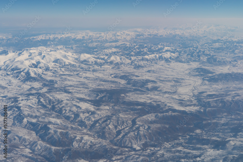 Fototapeta premium Wing of aerial view of an airplane jet flying above clouds from the window in traveling and transportation concept. White snow mountain in winter season. Nature landscape background.