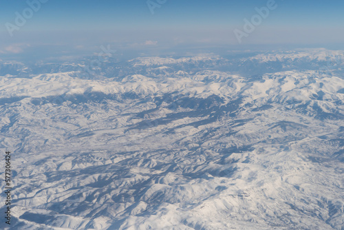 Wing of aerial view of an airplane jet flying above clouds from the window in traveling and transportation concept. White snow mountain in winter season. Nature landscape background.