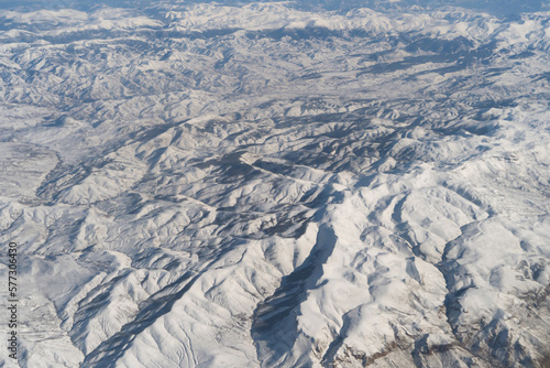 Wing of aerial view of an airplane jet flying above clouds from the window in traveling and transportation concept. White snow mountain in winter season. Nature landscape background.