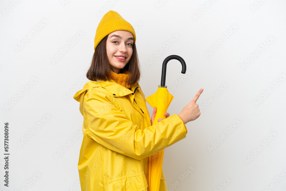 Young Ukrainian woman with rainproof coat and umbrella isolated on white background pointing back Young Ukrainian woman with rainproof coat and umbrella isolated on white background pointing back