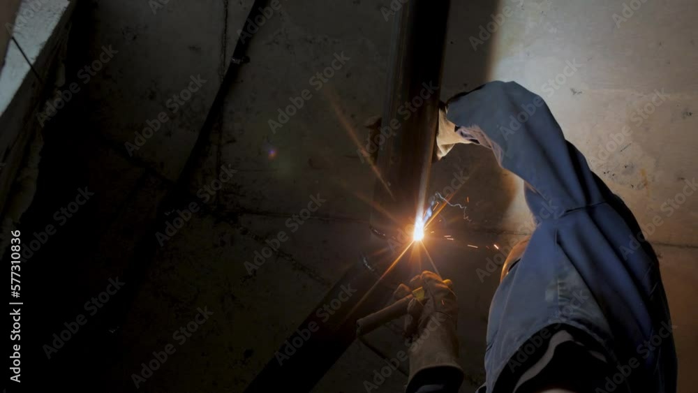 Skilled welder connects metal pipes with flame under hall ceiling close bottom shot. Construction site dangerous processes Skilled welder connects metal pipes with flame under hall ceiling close bottom shot. Construction site dangerous processes