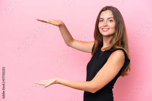 Young caucasian woman isolated on pink background holding copyspace to insert an ad © luismolinero