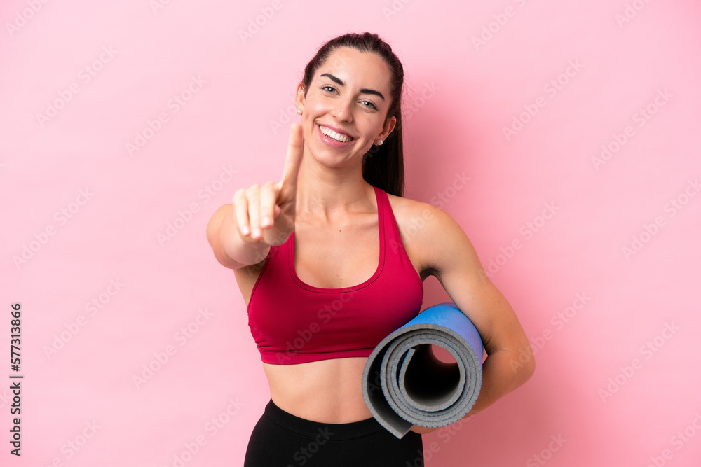 Young sport caucasian woman going to yoga classes while holding a mat isolated on pink background showing and lifting a finger Young sport caucasian woman going to yoga classes while holding a mat isolated on pink background showing and lifting a finger