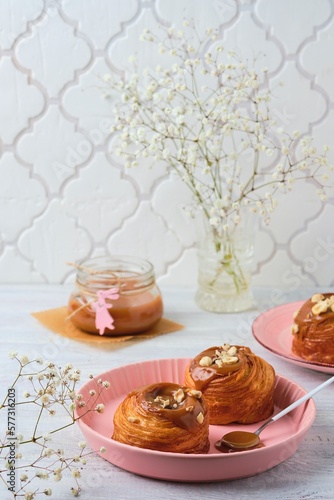 Yeast dough cruffins with salted caramel and hazelnuts in a pink baking dish on a light wooden background.