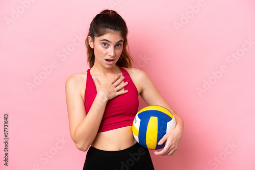 Young caucasian woman playing volleyball isolated on pink background surprised and shocked while looking right