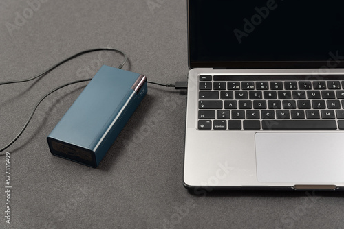 Top view laptop is connected by cord to an external battery. Laptop is charged by powerbank
