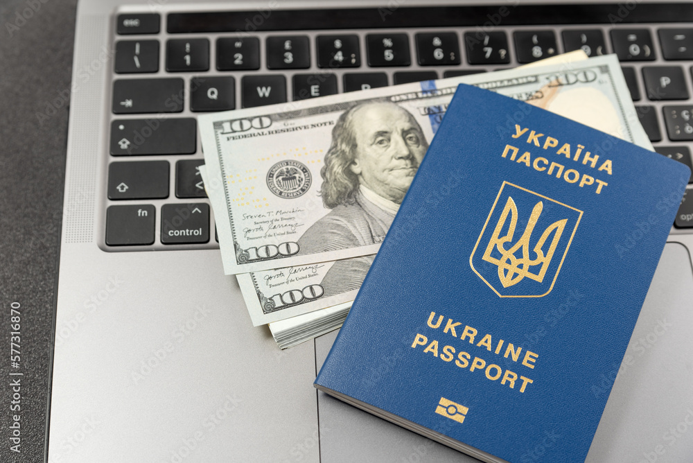 Fototapeta premium Ukrainian passport, cash dollars and a laptop. Online work for Ukrainians. Registration of documents online in Ukraine. Cash payments to Ukrainians.
