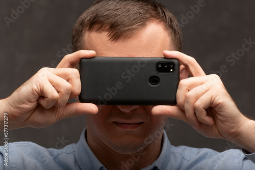 Close up portrait of man with phone near his face. Young man on gray background holding mobile smartphone near eyes.