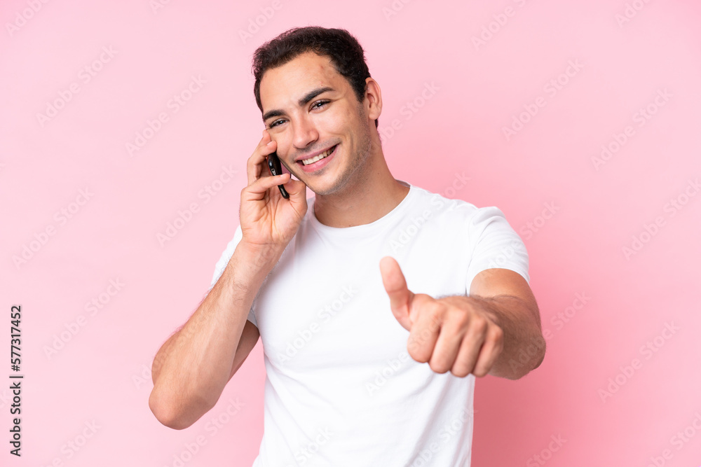 Young caucasian man isolated on pink background keeping a conversation with the mobile while doing thumbs up Young caucasian man isolated on pink background keeping a conversation with the mobile while doing thumbs up