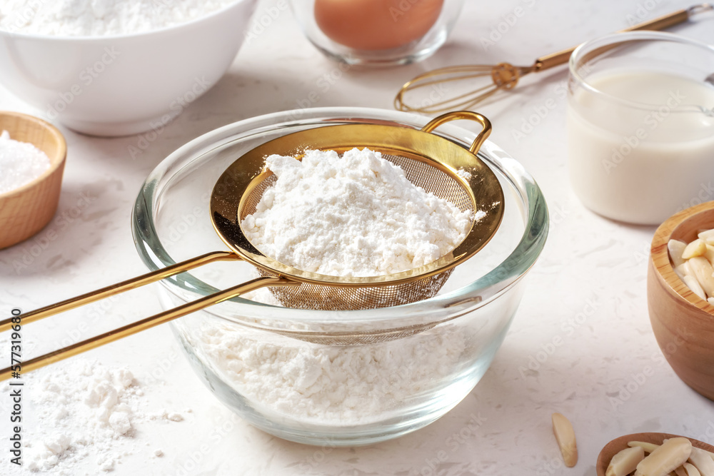 Sifting flour with gold sieve in glass bowl, closeup Sifting flour with gold sieve in glass bowl, closeup