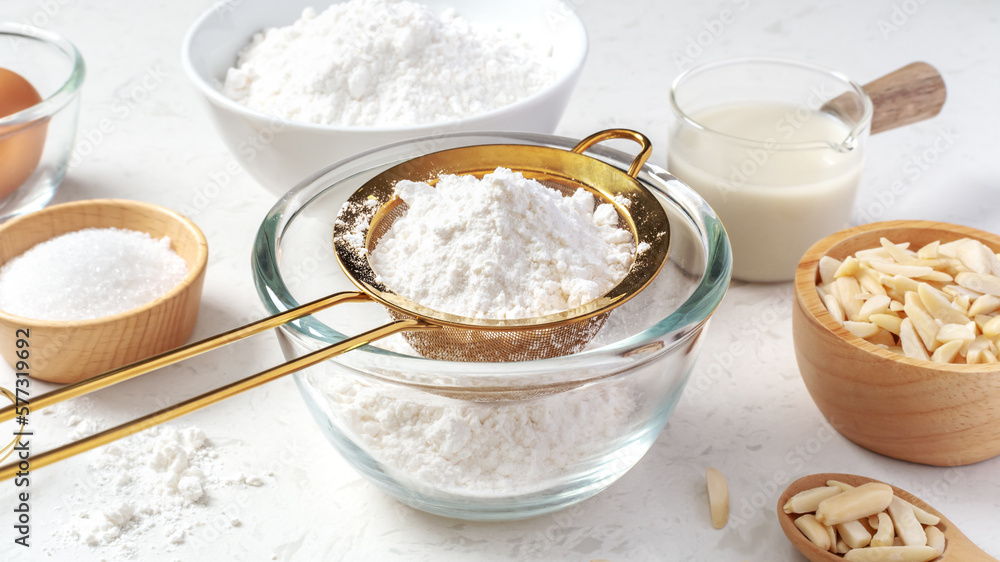 Sifting flour with gold sieve in glass bowl with cake or bakery ingredients on marble kitchen table