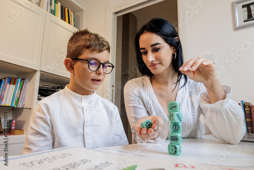 Educatrice con i capelli  scuri applica delle tecniche di apprendimento con un bambino biondo , all'interno di  in uno studio. privato. photo