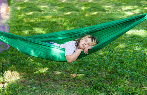 A little girl is sleeping in green hammock outside in the forest with bright grass. Summer time nap