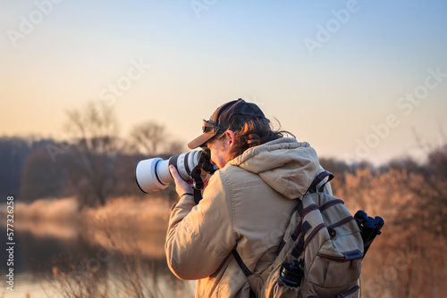 Wildlife photographer with camera photographing bird on lake at sunset