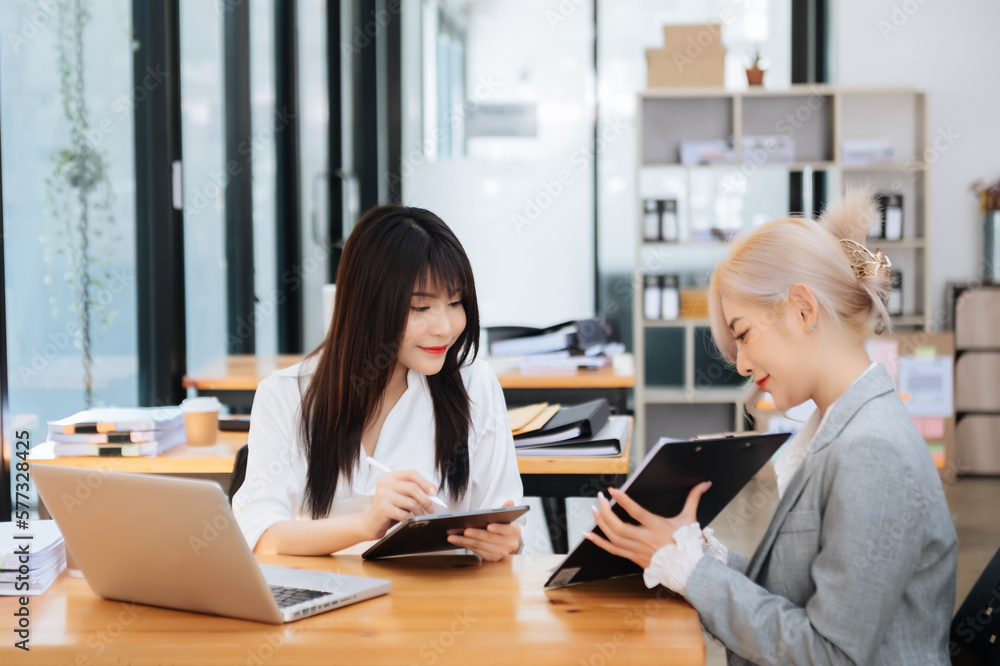 Two Asian businesswoman discuss investment project working and planning strategy with tablet laptop computer in office... Two Asian businesswoman discuss investment project working and planning strategy with tablet laptop computer in office...