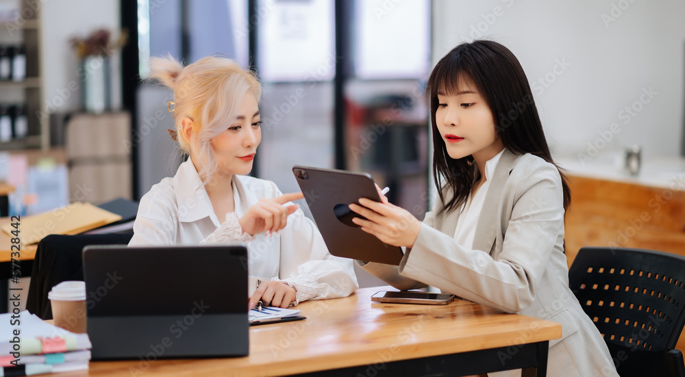 Two Asian businesswoman discuss investment project working and planning strategy with tablet laptop computer in office... Two Asian businesswoman discuss investment project working and planning strategy with tablet laptop computer in office...