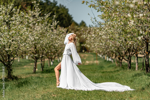 Blond blooming garden. A woman in a white dress walks through a blossoming cherry orchard. Long dress flies to the sides,