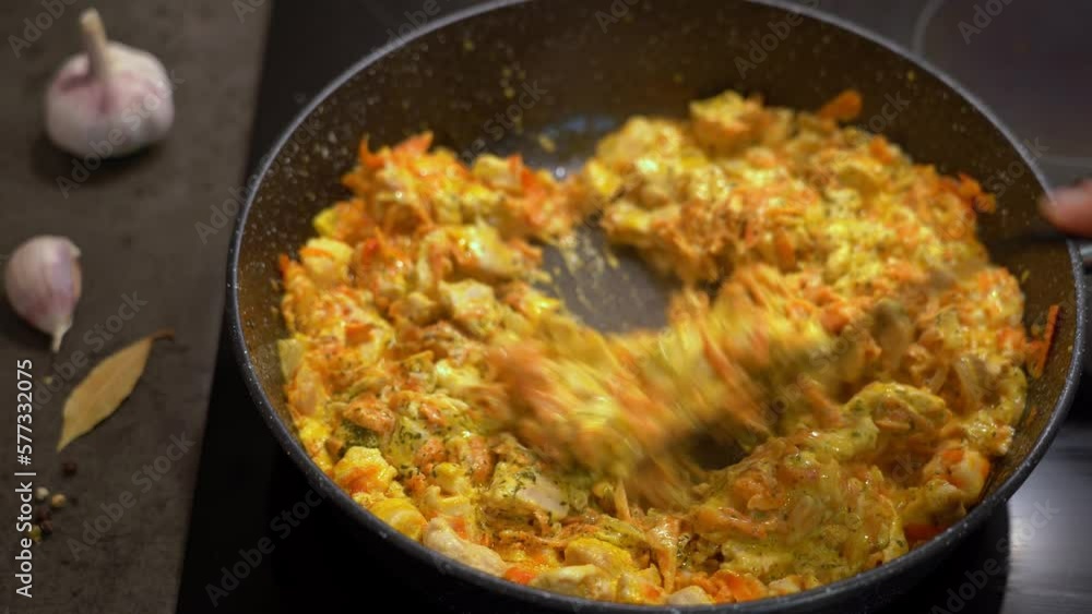Kitchen spatula stirs chicken in sauce curry with vegetables and spices in pan on stove. Meat is cooked with onions, carrot garlic. Indian food Kitchen spatula stirs chicken in sauce curry with vegetables and spices in pan on stove. Meat is cooked with onions, carrot garlic. Indian food