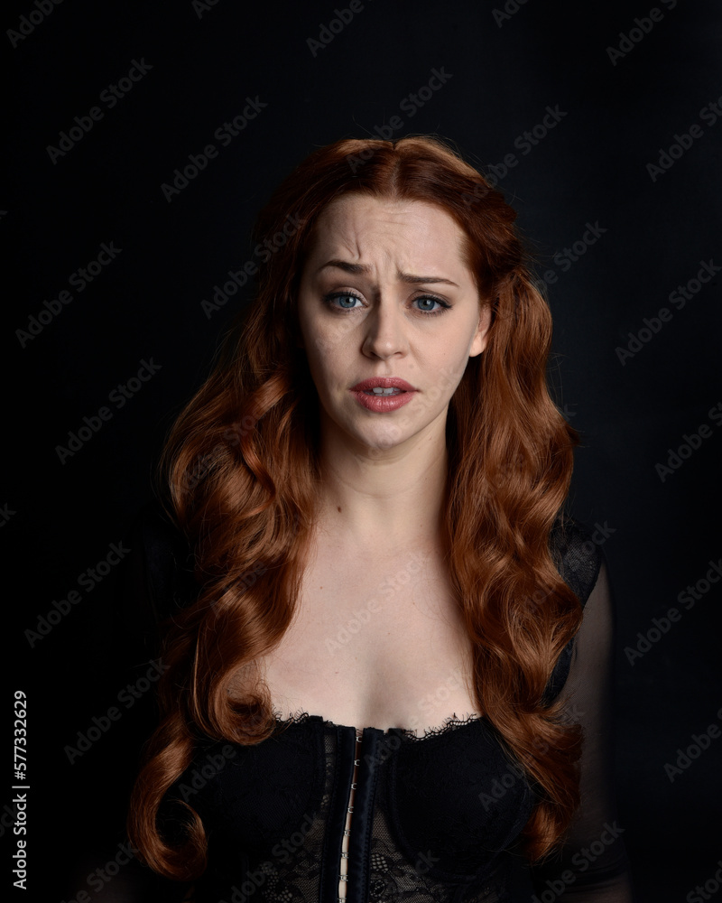 close up portrait of beautiful woman with long red hair wearing sheer corset top. variety of facial expressions, Isolated on dark studio background with moody silhouette lighting. close up portrait of beautiful woman with long red hair wearing sheer corset top. variety of facial expressions, Isolated on dark studio background with moody silhouette lighting.