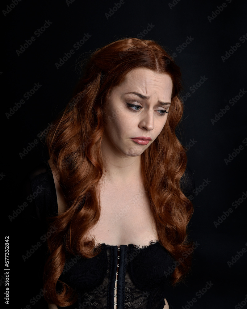 close up portrait of beautiful woman with long red hair wearing sheer corset top. variety of facial expressions,  Isolated on dark studio background with moody silhouette lighting.