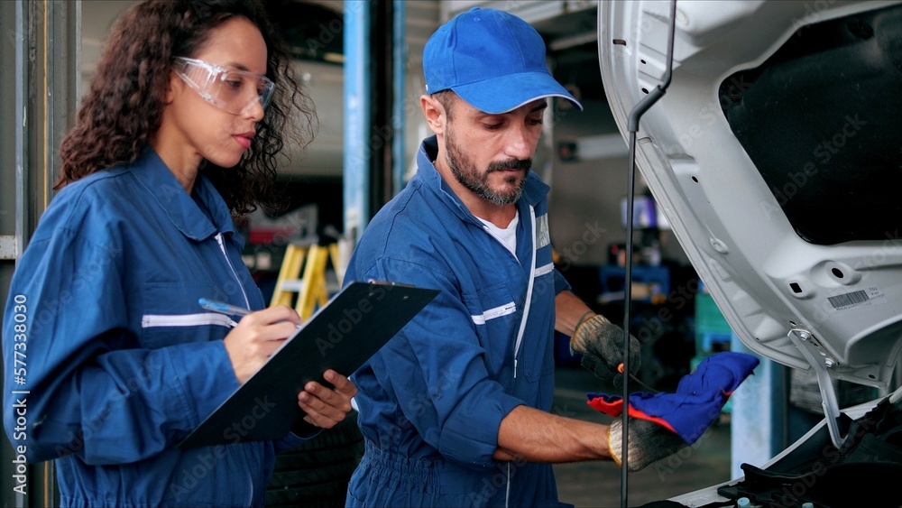 Two Auto mechanic checking car engine oil in car auto repair service center. Car repair and maintenance. Car mechanic working at automotive service center Two Auto mechanic checking car engine oil in car auto repair service center. Car repair and maintenance. Car mechanic working at automotive service center