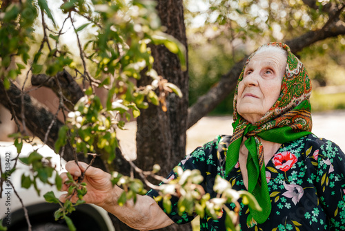 pretty portrait of an elderly woman dressed in a bathrobe and scarf posing for a photo near an old tree in her yard
