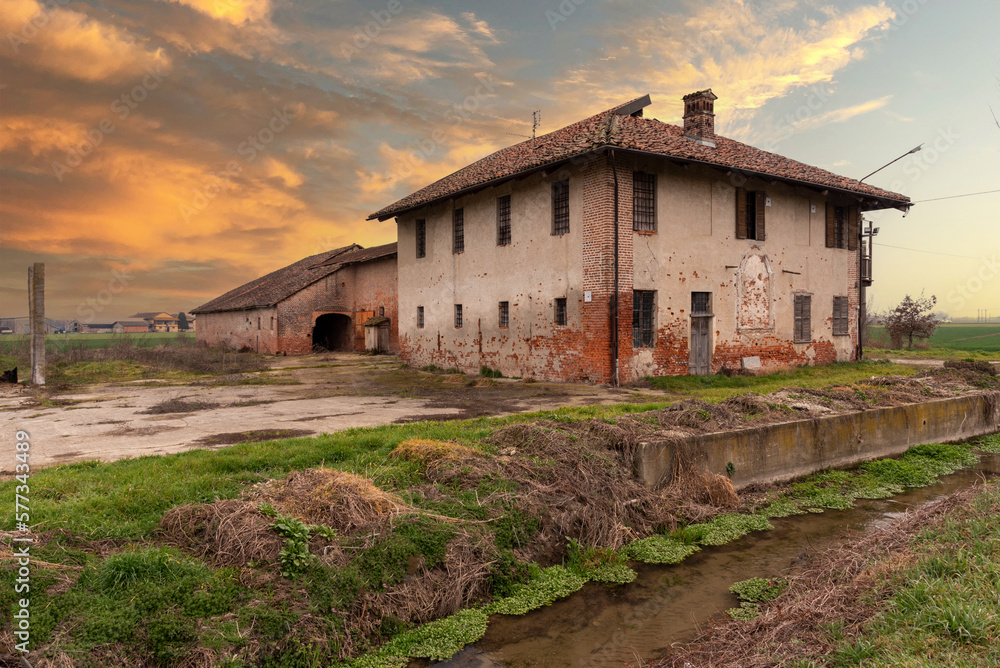 Old abandoned farmhouse with typical rural architecture of the Po Valley in the province of Cuneo, Italy, at sunset