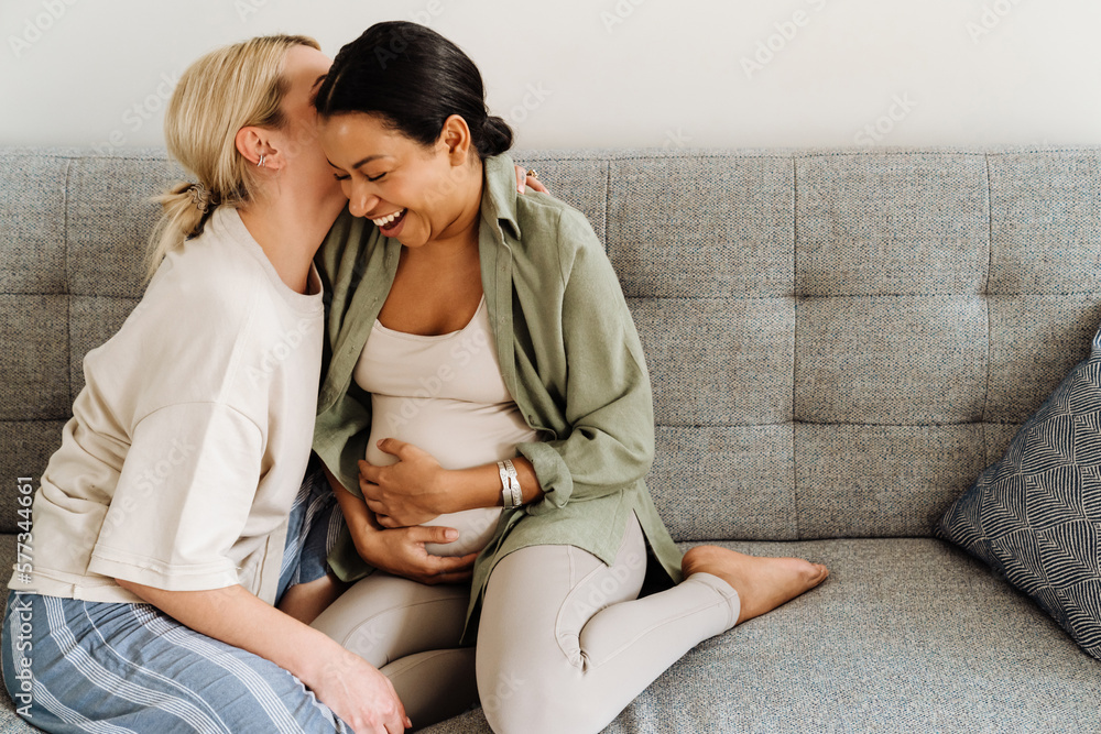 Woman kissing her pregnant wife while sitting on sofa Woman kissing her pregnant wife while sitting on sofa
