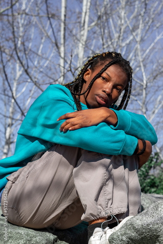 Mujer joven de color y trenzas en el pelo vestida en chándal sentada en las piedras en un parque de Madrid con la mirada perdida. photo