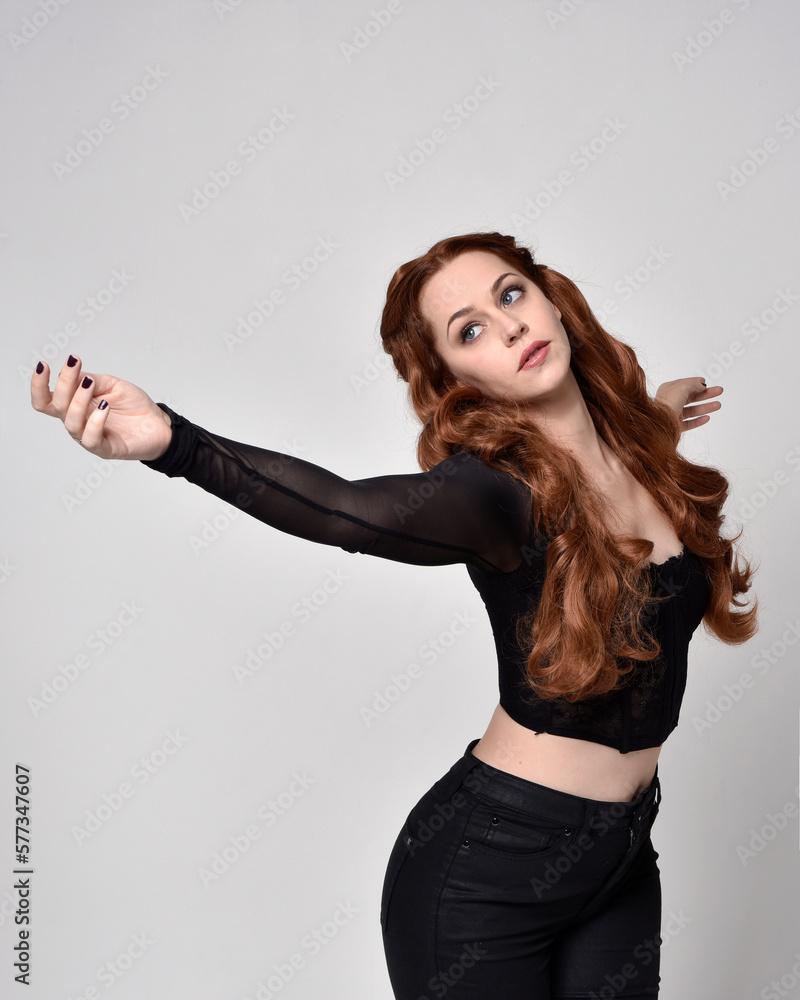 close up portrait of beautiful woman with red hair wearing sheer corset top, leather pants. Posing with gestural hands reaching out. Isolated on white studio background.