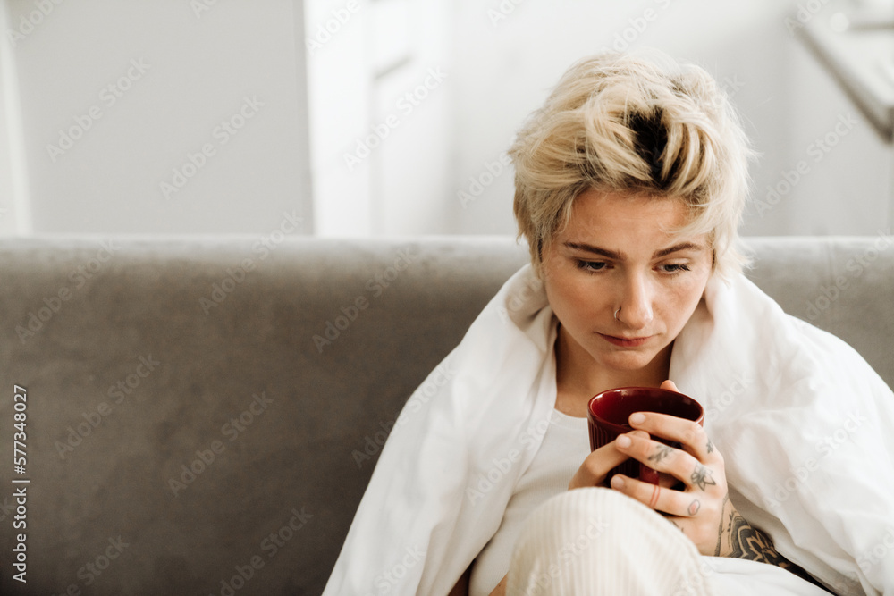 Depressed woman drinking tea while sitting on sofa at home Depressed woman drinking tea while sitting on sofa at home