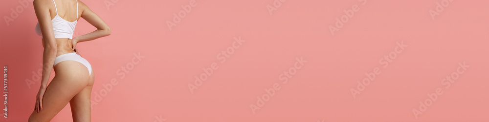 Back view. Cropped image of slim woman with perfect body shape in underwear posing over pink background. Concept of beauty, body and skin care, health, anti-cellulite program Back view. Cropped image of slim woman with perfect body shape in underwear posing over pink background. Concept of beauty, body and skin care, health, anti-cellulite program