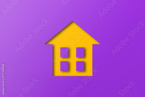 Yellow paper cut out house shape isolated on purple paper background.