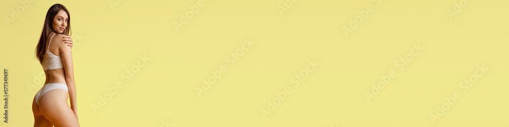 Fototapeta premium Pretty young girl posing in cotton underwear over yellow studio background. Weight loss. Concept of beauty, body and skin care, fitness, health, spa, cosmetics, ad