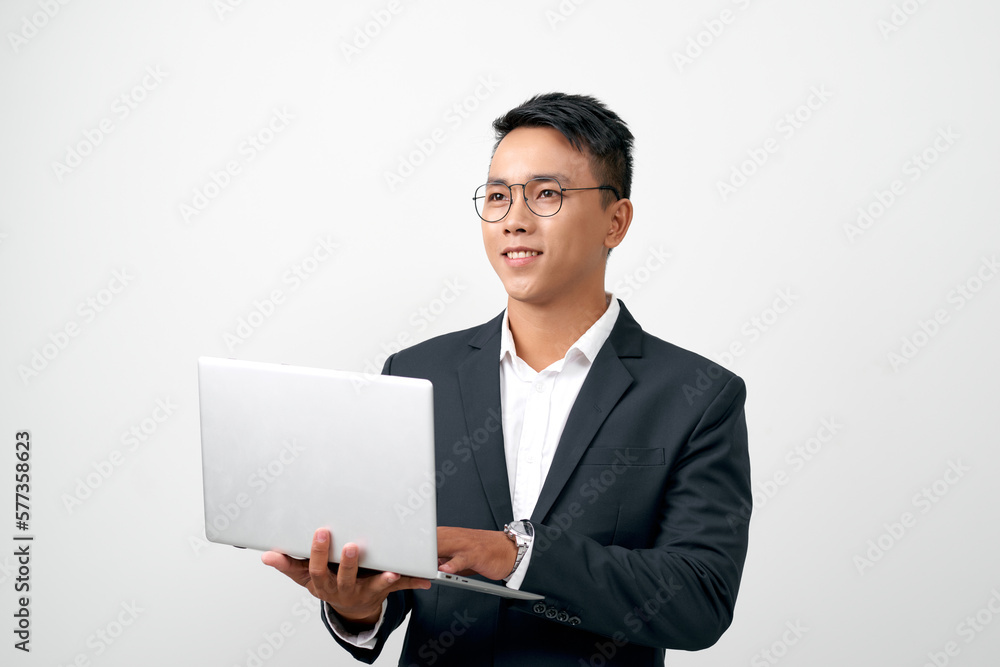 Confident young handsome man in black suit holding open grey laptop and smiling while standing Confident young handsome man in black suit holding open grey laptop and smiling while standing