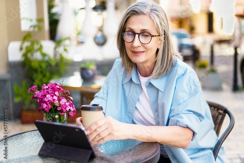 Wall Mural silver-haired mature European woman sitting at an outdoor cafe, smiling with joy as she looks at her tablet PC