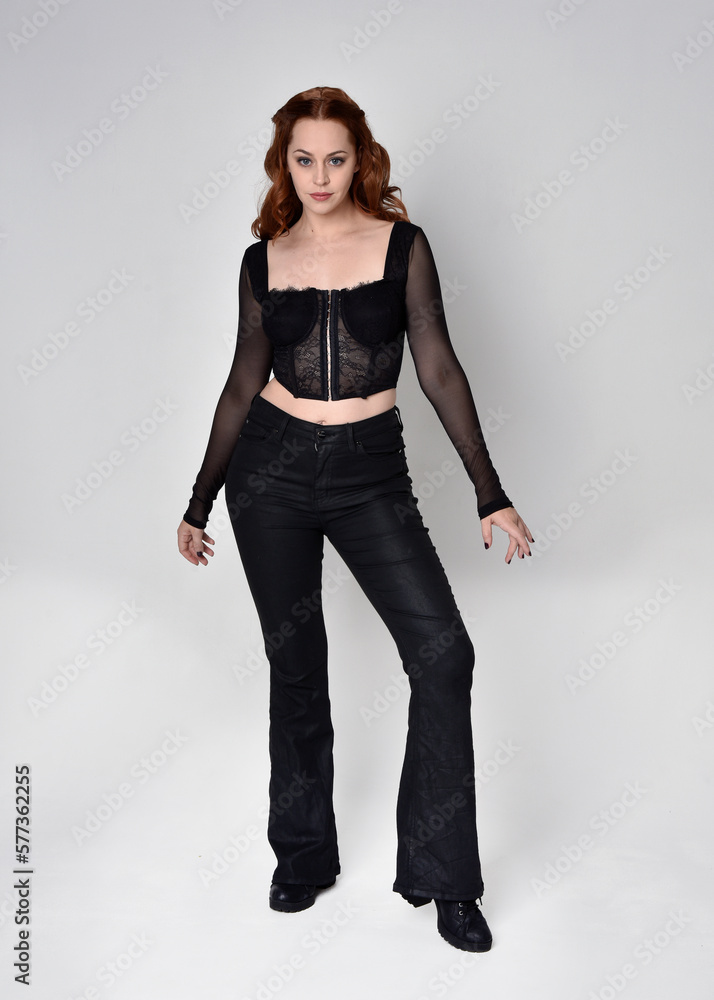 Full length portrait of beautiful woman with long red hair wearing black corset top and leather pants. Standing pose, walking forwards with gestural hands reaching out. Isolated on white studio backgr Full length portrait of beautiful woman with long red hair wearing black corset top and leather pants. Standing pose, walking forwards with gestural hands reaching out. Isolated on white studio backgr