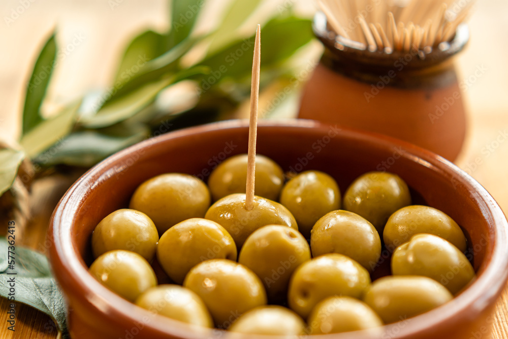 Close-up of a clay jar with olives and a toothpick stuck in it with the background out of focus. Typical Spanish food. With copy space Close-up of a clay jar with olives and a toothpick stuck in it with the background out of focus. Typical Spanish food. With copy space