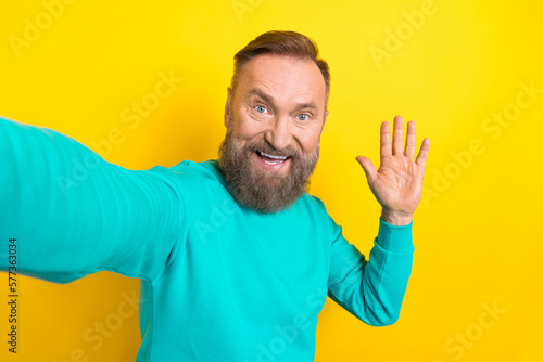 Photo portrait of attractive grandpa make selfie streaming wave hand dressed stylish cyan garment isolated on yellow color background