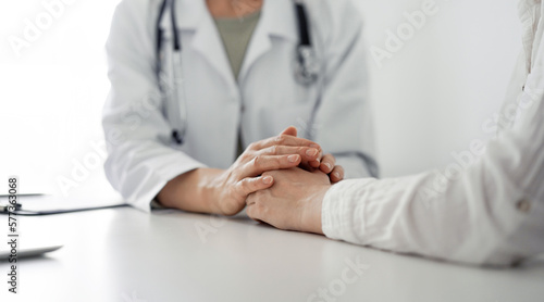 Doctor and patient sitting at the desk in clinic office. The focus is on female physician's hands reassuring woman, close up. Perfect medical service, empathy, and medicine concept.