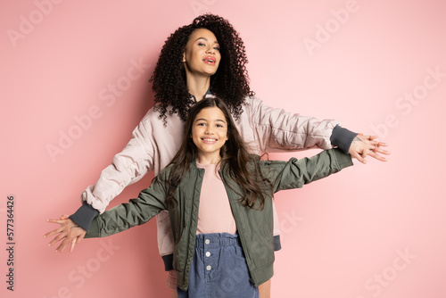 Stampa su tela Curly mother holding hands of cheerful daughter on pink background